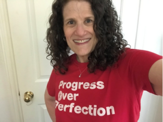 A selfie of Meryl Evans wearing a red T-shirt that says 'Progress Over Perfection'